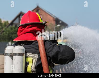 Pompier en uniforme et masque à oxygène, pulvériser de l'eau. Banque D'Images