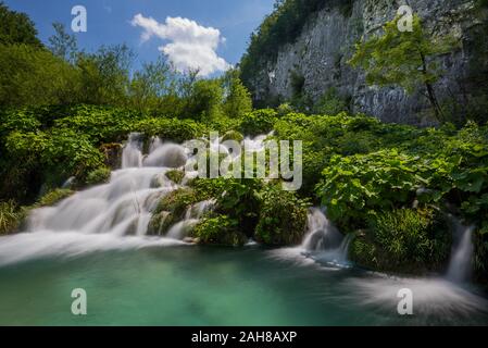 Vue panoramique sur une cascade croate entourée de végétation sous un ciel bleu avec des nuages puffés dans le parc naturel de Plitvice Banque D'Images