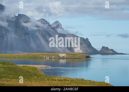 Vue grand angle d'un paysage islandais avec une chaîne de montagnes penchant dans la mer, sous un ciel bleu avec des nuages puffés Banque D'Images