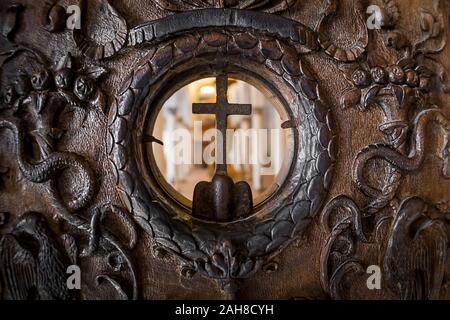 Fermeture symétrique d'une ancienne porte en bois incrusté avec une ouverture circulaire et une croix chrétienne au milieu Banque D'Images