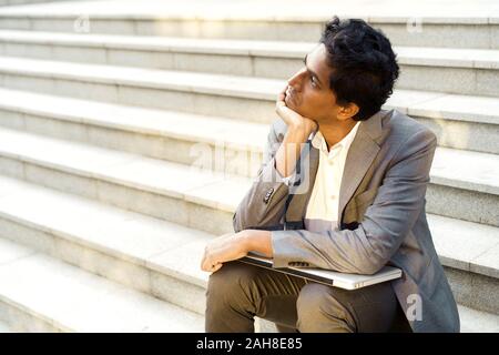 Beau jeune homme indien dans un bureau costume et chemise blanche assise sur les marches Banque D'Images