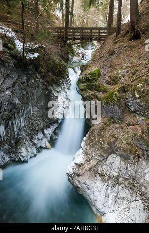 Vue à grand angle d'une chute d'eau de montagne en streaming sous un pont en bois et entre les roches blanches, entourées d'arbres et de brousse Banque D'Images