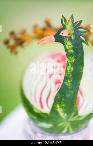 Gros plan d'une pastèque sculptée comme un paon contre arrière-plan bokeh vert Banque D'Images