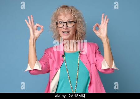 Smiling senior dame en gesticulant lunettes signe ok parfait Banque D'Images