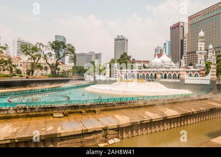 Kuala Lumpur, Malaisie - le 5 mars 2019 : Le Masjid Jamek (mosquée du vendredi), de la gare et du centre-ville d'édifices modernes donnent sur la rivière Chicago. Banque D'Images