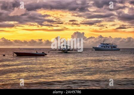 Un lever du soleil tropical, scène avec trois bateaux de touristes amarré dans un calme resort anchorage aux Philippines. Banque D'Images