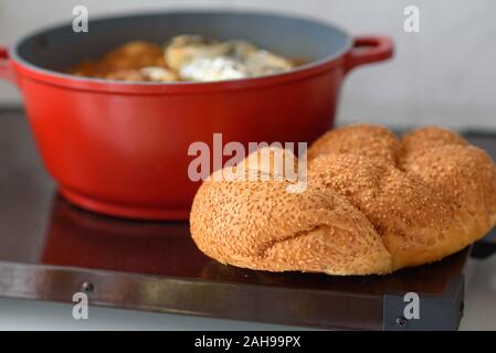 La plaque chaude pour le Sabbat, un pot de viande épicé cuit avec pommes de terre, blé, orge et d'œufs. Pot de tcholent Hamin en hébreu, challah-pain spécial dans une cuisine juive. La nourriture traditionnelle Shabbat juif. Banque D'Images