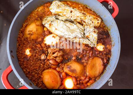 La plaque chaude pour le Sabbat, un pot de viande épicé cuit avec pommes de terre, blé, orge et d'œufs. Pot de tcholent Hamin en hébreu, challah-pain spécial dans une cuisine juive. La nourriture traditionnelle Shabbat juif. Banque D'Images