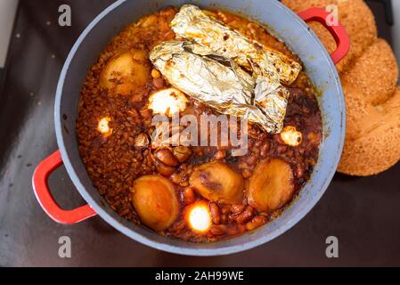 La plaque chaude pour le Sabbat, un pot de viande épicé cuit avec pommes de terre, blé, orge et d'œufs. Pot de tcholent Hamin en hébreu, challah-pain spécial dans une cuisine juive. La nourriture traditionnelle Shabbat juif. Banque D'Images