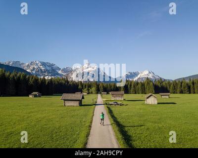 Female hiker sur un sentier, granges à foin dans un pré, et les montagnes, d''Ehrwalder Sonnenspitz près de Ehrwald, Mieminger Kette, Tyrol, Autriche Banque D'Images