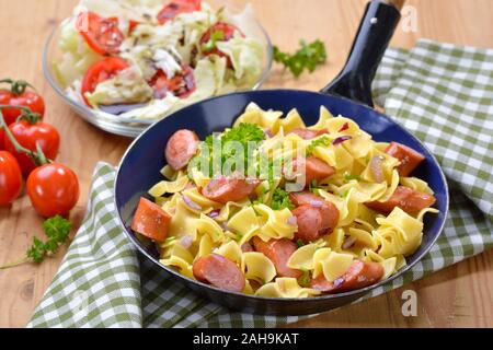 Repas autrichien avec des pâtes et saucisses frites, appelées Wurstfleckerl, servi dans une poêle avec une petite salade avec l'huile de graines de potiron de Styrie Banque D'Images