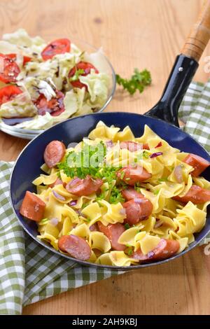 Repas autrichien avec des pâtes et saucisses frites, appelées Wurstfleckerl, servi dans une poêle avec une petite salade avec l'huile de graines de potiron de Styrie Banque D'Images