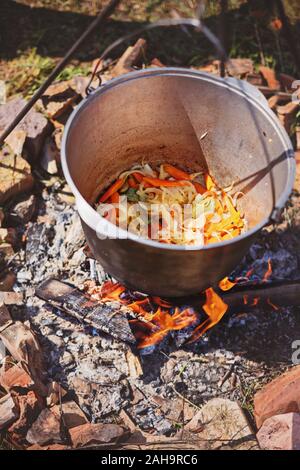 Ragoût de légumes à la cuisson en grand chaudron sur feu de camping. Journée ensoleillée Banque D'Images