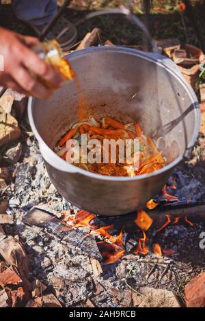 Verser les épices en légumes ragoût. Cuire le dîner en grand chaudron sur feu de camping. Journée ensoleillée Banque D'Images