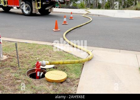 Feu jaune rouge flexible raccordé au robinet d'eau dans le sol et l'extension de l'autre côté de la route Banque D'Images