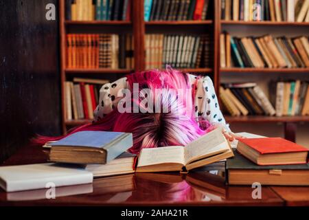 Femme aux cheveux roses endormi à une table avec des livres dans la bibliothèque Banque D'Images