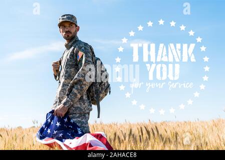 Soldat en uniforme tenant drapeau américain en étant debout dans le champ avec nous vous remercions pour votre service illustration Banque D'Images