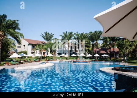 Parasols et transats sont placés dans la piscine. Les palmiers sont plantés côte à côte à l'extérieur de la piscine. Banque D'Images