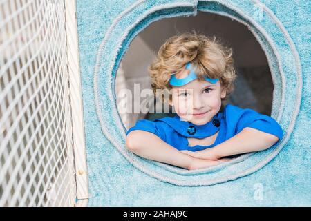 Curly blonde petit garçon en costume bleu de Superman dans la fenêtre ronde Banque D'Images