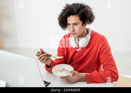 Jeune homme freelancer avoir muesli avec lait et regarder la vidéo en ligne Banque D'Images