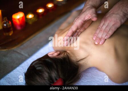 Les mains des hommes faire un massage du cou thérapeutiques pour une fille allongée sur une table de massage. Des bougies sur l'arrière-plan. Santé et elax concept. Banque D'Images