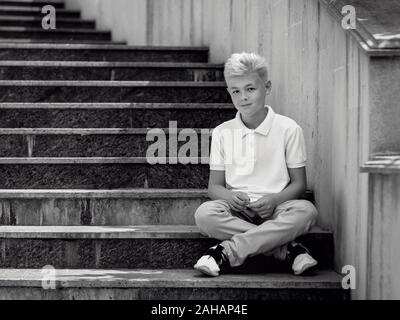 Portrait monochrome (noir et blanc) de joli beau blond onze vieux garçon (adolescent) assis sur les escaliers extérieur.Grandir, puérile, séparation Banque D'Images