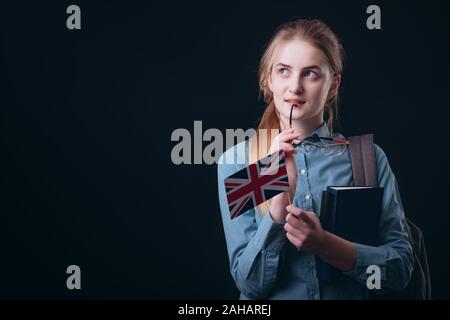 Portrait d'une jeune fille rêveuse étudiant gingembre avec drapeau britannique à côté et vers le haut fond sombre copyspace isolé Banque D'Images