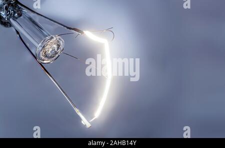 Filament de lampe à incandescence lumineuse close-up sur fond gris Banque D'Images