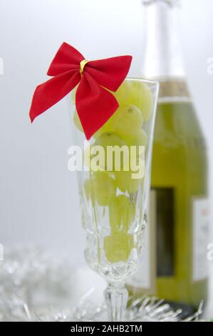 Un verre plein de raisins, dans l'arrière-plan une bouteille de vin mousseux pour célébrer la fin de l'année et le début d'une meilleure Banque D'Images
