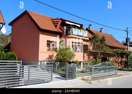 Petite maison de famille de banlieue rénové avec nouvelle façade rose foncé et haut balcon rempli de fleurs entouré de plantes de jardin et clôture métallique next Banque D'Images