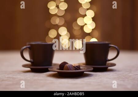 Deux tasses et soucoupes marron avec feux lumineux au-dessus d'eux et une plaque de chocolat saupoudré de cacao. Banque D'Images