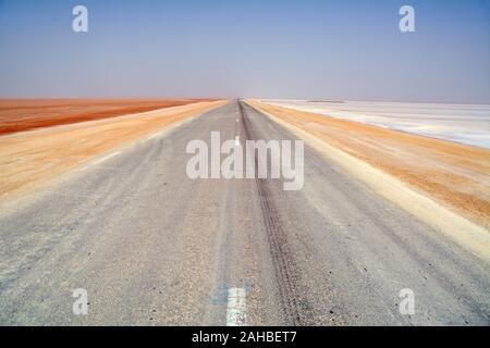 Une route qui traverse le lac de sel coloré de Chott el Djerid près de la ville de Tozeur dans le désert du Sahara en Tunisie méridionale, Afrique du Nord. Banque D'Images