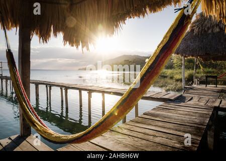 Hamac à quai pendant le coucher du soleil avec des rayons de soleil au lac de rétroéclairage Itza, El Remate, Peten, Guatemala Banque D'Images