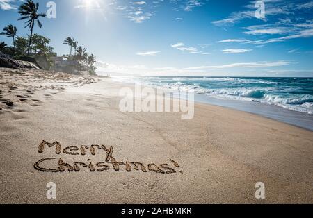 Joyeux Noël et écrit dans le sable sur Sunset Beach à Hawaii avec palmiers et l'océan en arrière-plan Banque D'Images