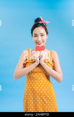 Young woman in casual dress posing avec coeur rouge isolé sur fond bleu Banque D'Images