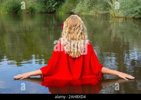 Jeune femme blonde en rouge dans l'eau naturelle de marche de liage Banque D'Images