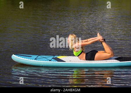 Blond caucasian woman practicing yoga posture sur le SUP en rivière Banque D'Images