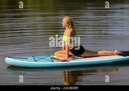 Jeune femme européenne dans le yoga posture swan on paddle board à l'eau Banque D'Images