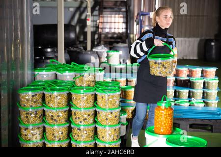 Femme au travail positif à l'entrepôt, l'empilement des conteneurs en plastique avec les olives sélectionnées Banque D'Images