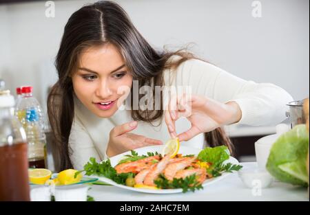 Smiling woman in pull à la décoration de la plaque avec sauté de crevettes à la maison cuisine Banque D'Images