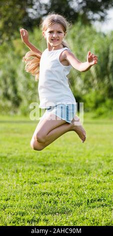 Heureuse petite fille à l'école élémentaire âge tournant on Green grass in park Banque D'Images