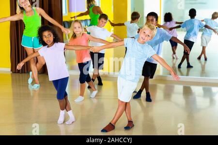 Groupe d'heureux joyeux enfants pratiquant des mouvements vigoureux dans la classe de danse jive avec entraîneur féminin Banque D'Images