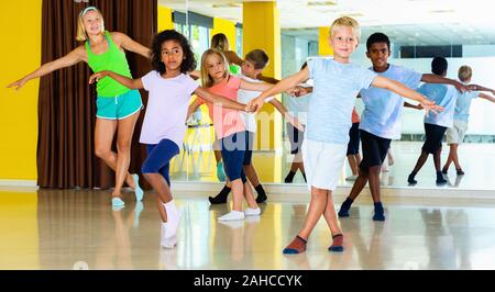 Groupe d'heureux joyeux enfants pratiquant positif des mouvements vigoureux jive dans classe de danse avec entraîneur féminin Banque D'Images