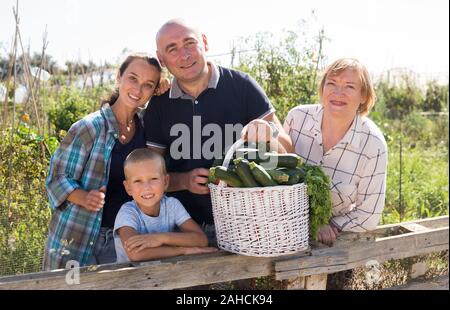 Saison de récolte. Portrait de couple avec enfant et femme mature jardiniers amateurs posant avec récolte de légumes sur le jardin ensoleillé Banque D'Images