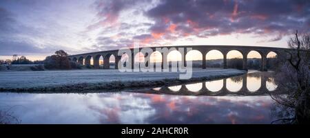 Un lever du soleil remplit le ciel derrière Arthington viaduc en basse Wharfedale, Yorkshire, qui se reflète dans les eaux calmes de la rivière Wharfe. Banque D'Images