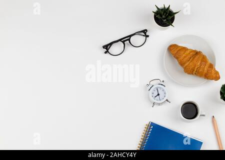 Matin d'affaires avec ordinateur portable bleu, tasse de café, croissant , horloge et verres sur fond blanc Vue de dessus immersive copie espace télévision lay Banque D'Images