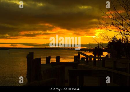 Silhouette de personnes, d'arbres et d'une jetée à l'eau grand coucher du soleil et la réflexion. Coucher de soleil sur un lac en Allemagne, Zingst. Banque D'Images