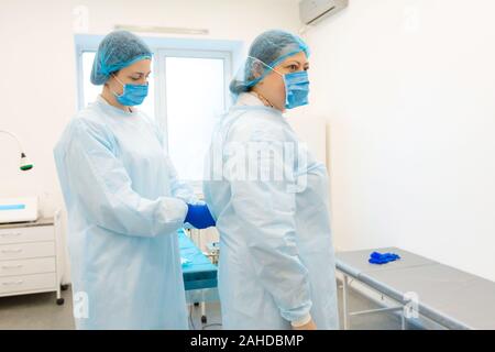 Une infirmière robes une chirurgien dans un costume stérile avant la chirurgie. Banque D'Images