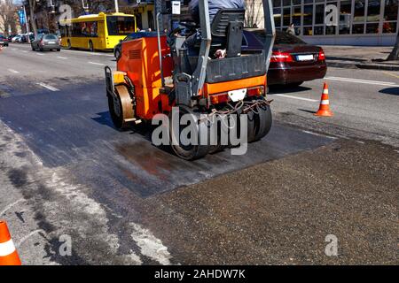 Un lourd rouleau vibrant orange compacts et les niveaux d'une section de route sur une rue de ville clôturé avec cônes de circulation, de droit avec l'exemplaire de l'espace. Banque D'Images