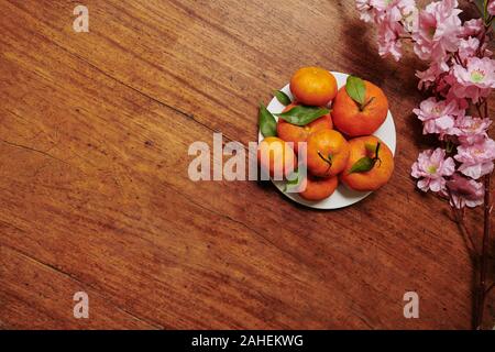 Branche de pêcher en fleurs et la plaque avec des mandarines mûres sur table en bois préparés pour le festival de printemps Banque D'Images